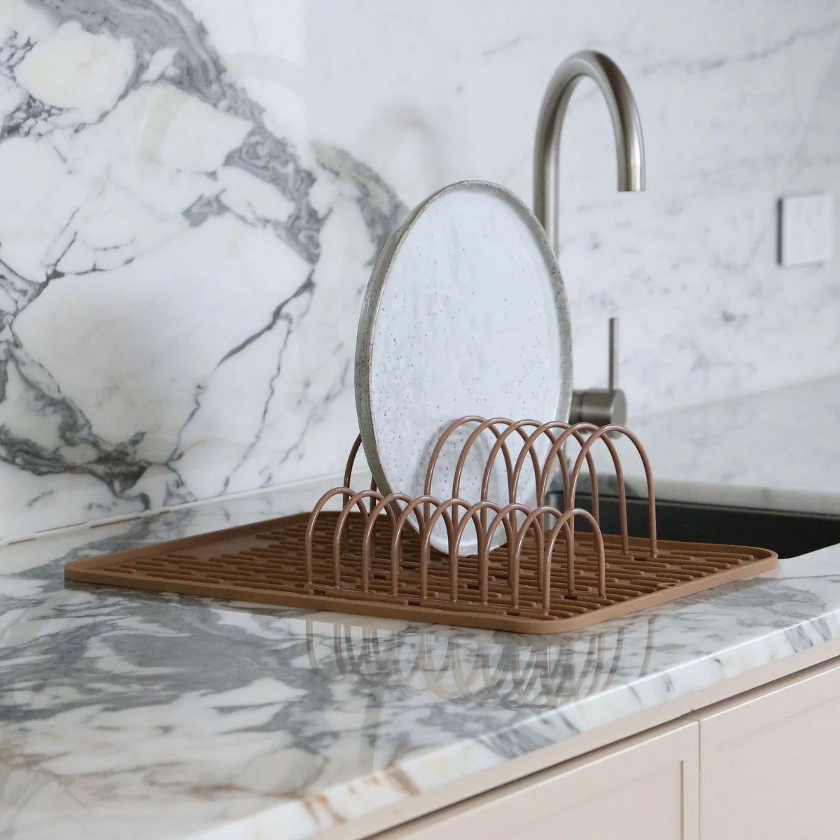 Dish drying rack on a marble kitchen counter with a sink in the background