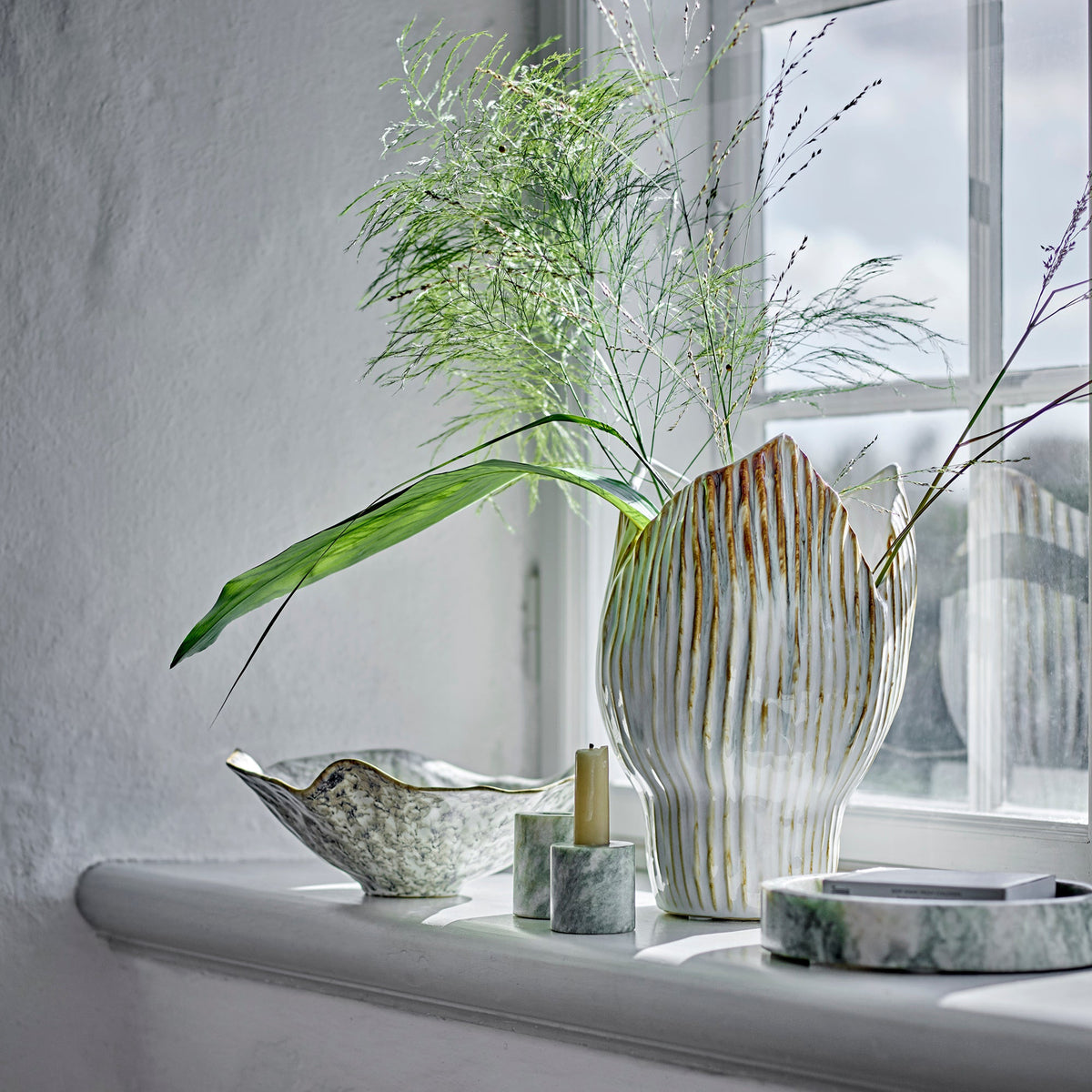 Decorative setting with a vase, candle, and bowls on a windowsill.