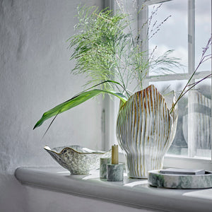 Decorative setting with a vase, candle, and bowls on a windowsill.