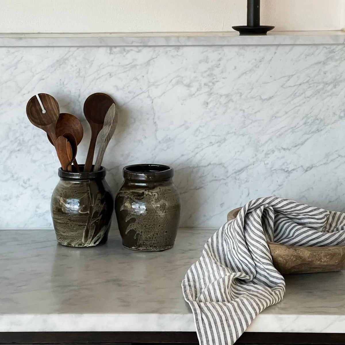 Kitchen counter with jars, wooden spoons, and a candle against a marble backsplash.