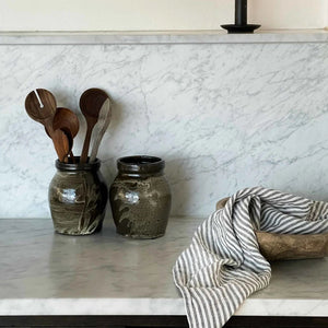 Kitchen counter with jars, wooden spoons, and a candle against a marble backsplash.