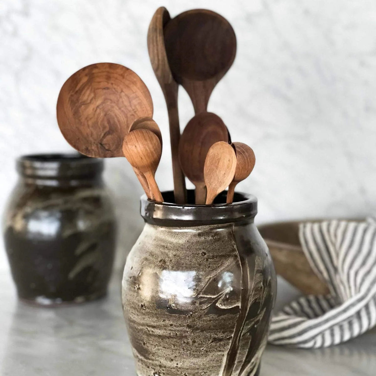 Set of wooden utensils in a rustic ceramic holder on a kitchen counter.