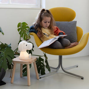 Child reading a book in a yellow chair with a small white lamp and plant nearby.