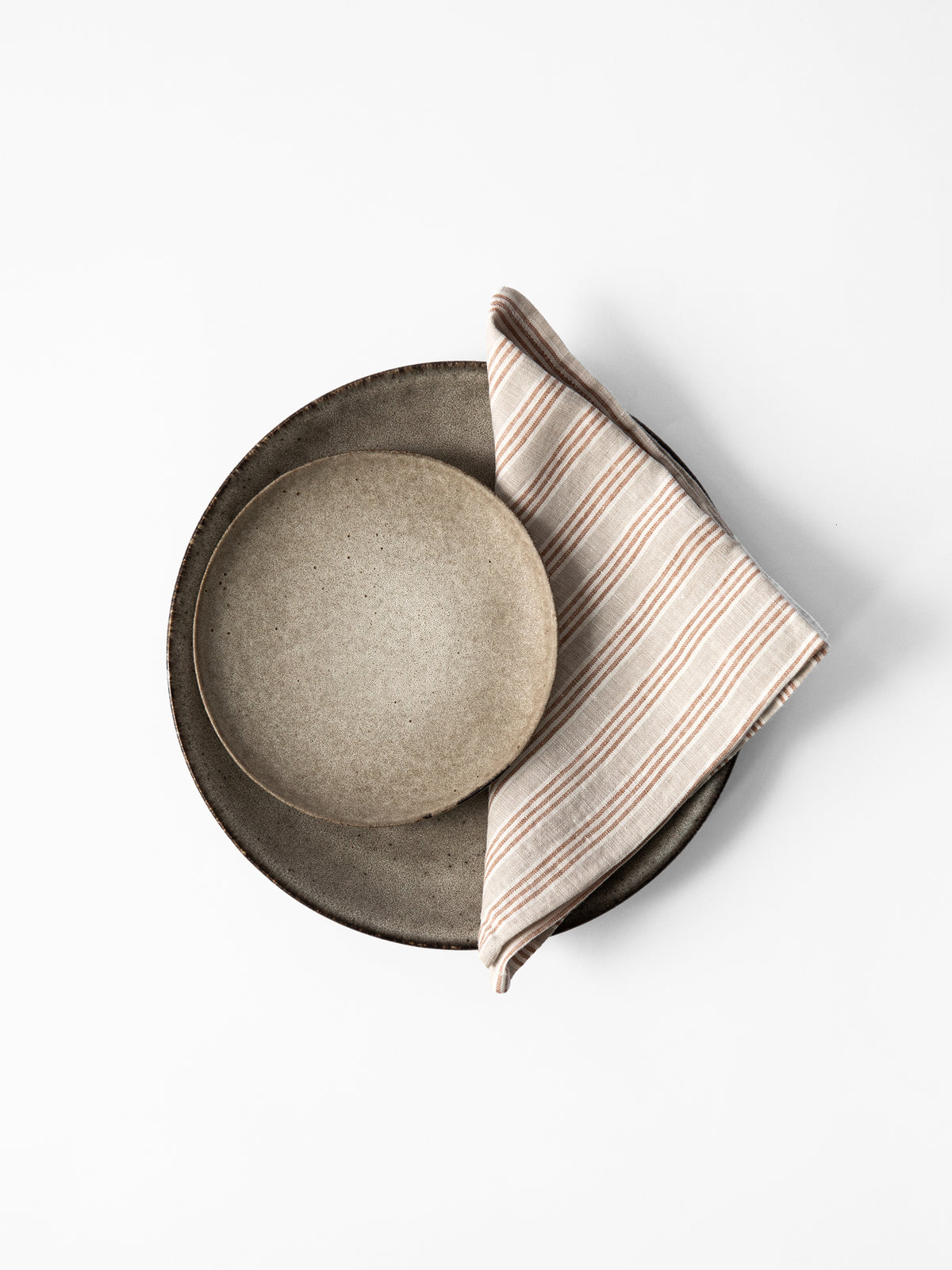 Set of ceramic plates with a striped Tell me more linen napkin on a white background