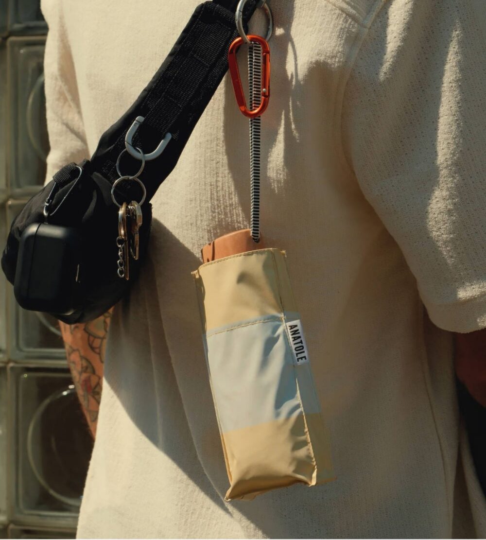 Beige umbrella with black handle and keychain attached to a person's shoulder.