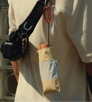 Beige umbrella with black handle and keychain attached to a person's shoulder.