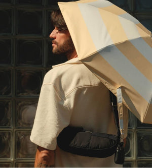Person holding a large striped Anatole umbrella against a glass block wall.