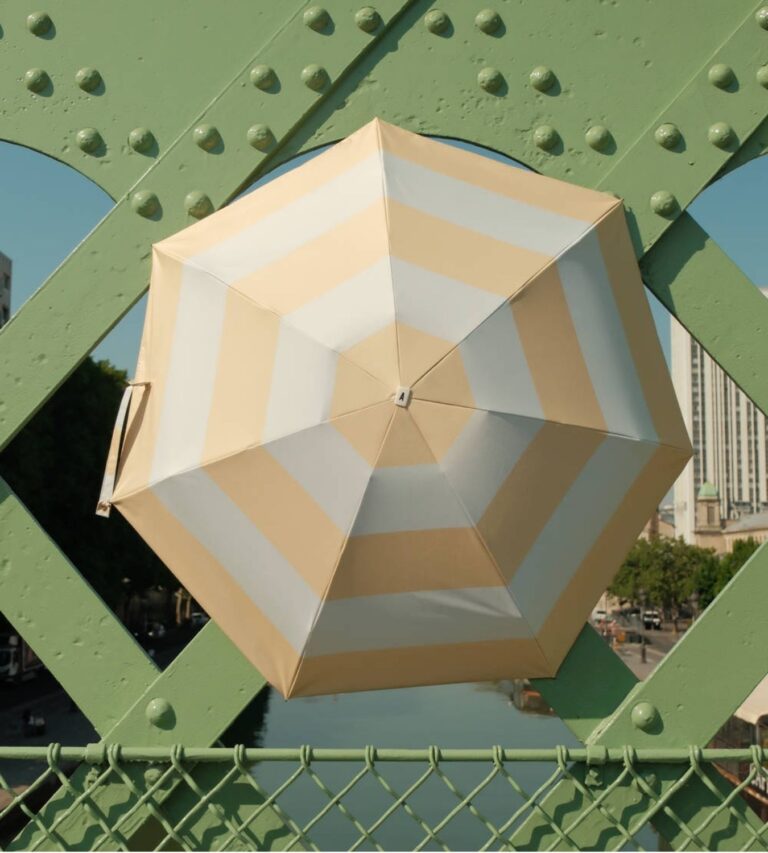 Hexagonal Anatole umbrella with beige and white stripes on a green metal structure.