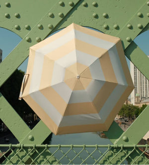 Hexagonal Anatole umbrella with beige and white stripes on a green metal structure.